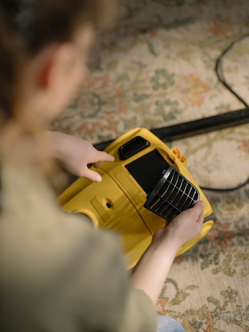 A professional cleaner wearing a full white protective suit, gloves, and a face mask is using a vacuum cleaner to deep clean a beige carpet in a bright, modern living room. The room features white wal